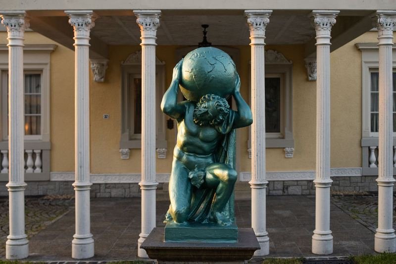 Bronzefigur des Atlas vor den Säulen eines historischen Gebäudes