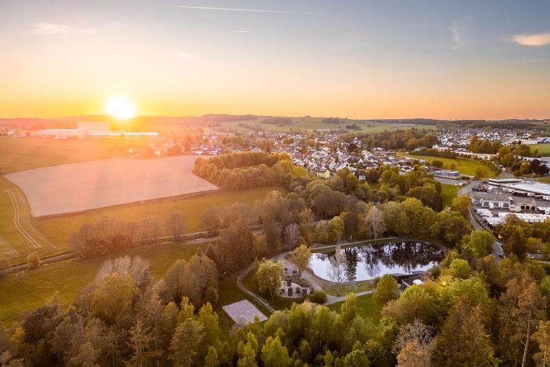 Luftbild einer Landschaft mit Teich und Wald im Abendlicht