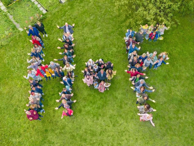 Drohnenaufnahme: Personen bilden auf einer Wiese die Buchstaben H und F