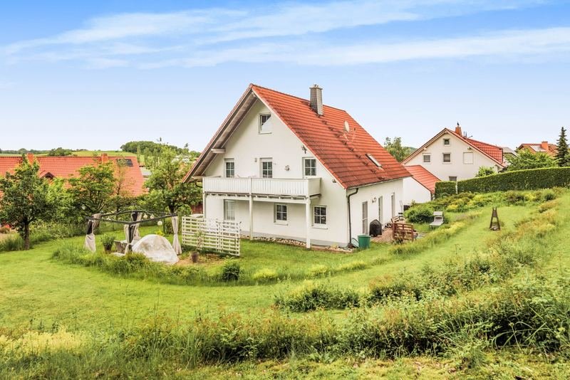 Einfamilienhaus mit rotem Dach und Garten unter blauem Himmel