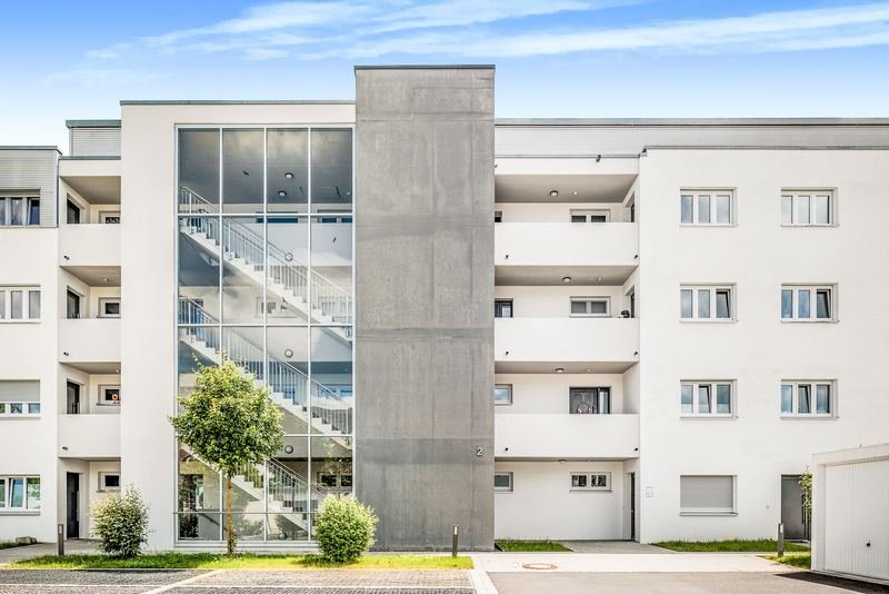 Wohnanlage mit verglastem Treppenhaus und Sichtbetonturm unter blauem Himmel