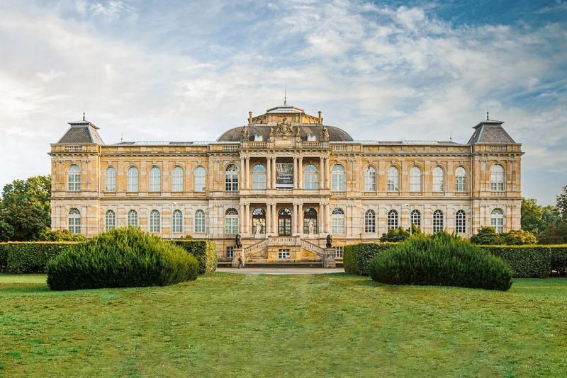 Historisches Gebäude mit Säulenportikus hinter gepflegtem Rasen und Hecken