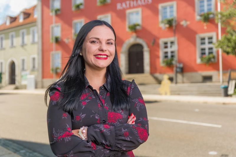 Businessporträt einer Frau mit verschränkten Armen vor einem roten Rathaus